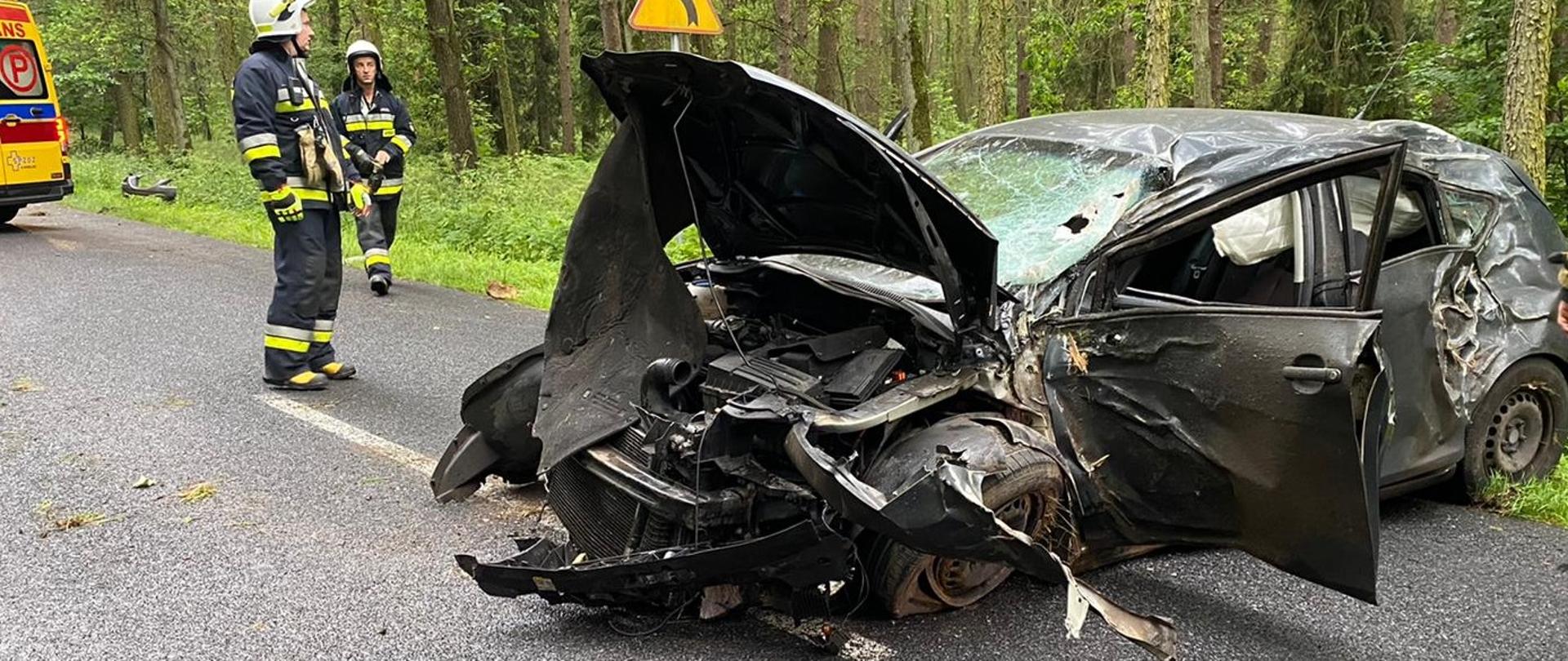 Rozbity samochód. Z lewej strony stoją strażacy i karetka pogotowia
