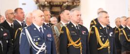 Przedstawiciele służb mundurowych w mundurach galowych stoją obok siebie w ławkach w kościele.