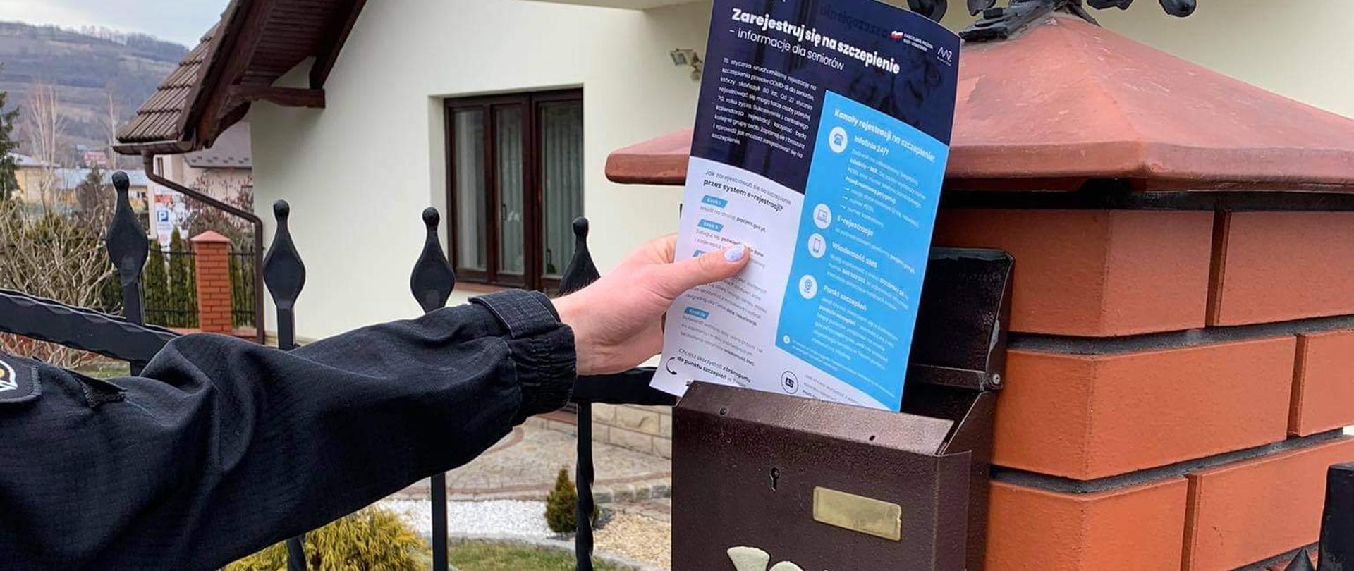 Strażak wrzuca ulotkę do skrzynki pocztowej zamontowanej na słupku ogrodzenia.