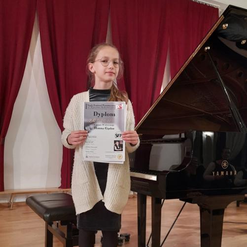 Uczennica stojąca przy fortepianie trzyma w rękach "brązowy" dyplom otrzymany w I Śląskim Festiwalu Pianistycznym im. Władysławy Markiewiczówny w Tarnowskich Górach