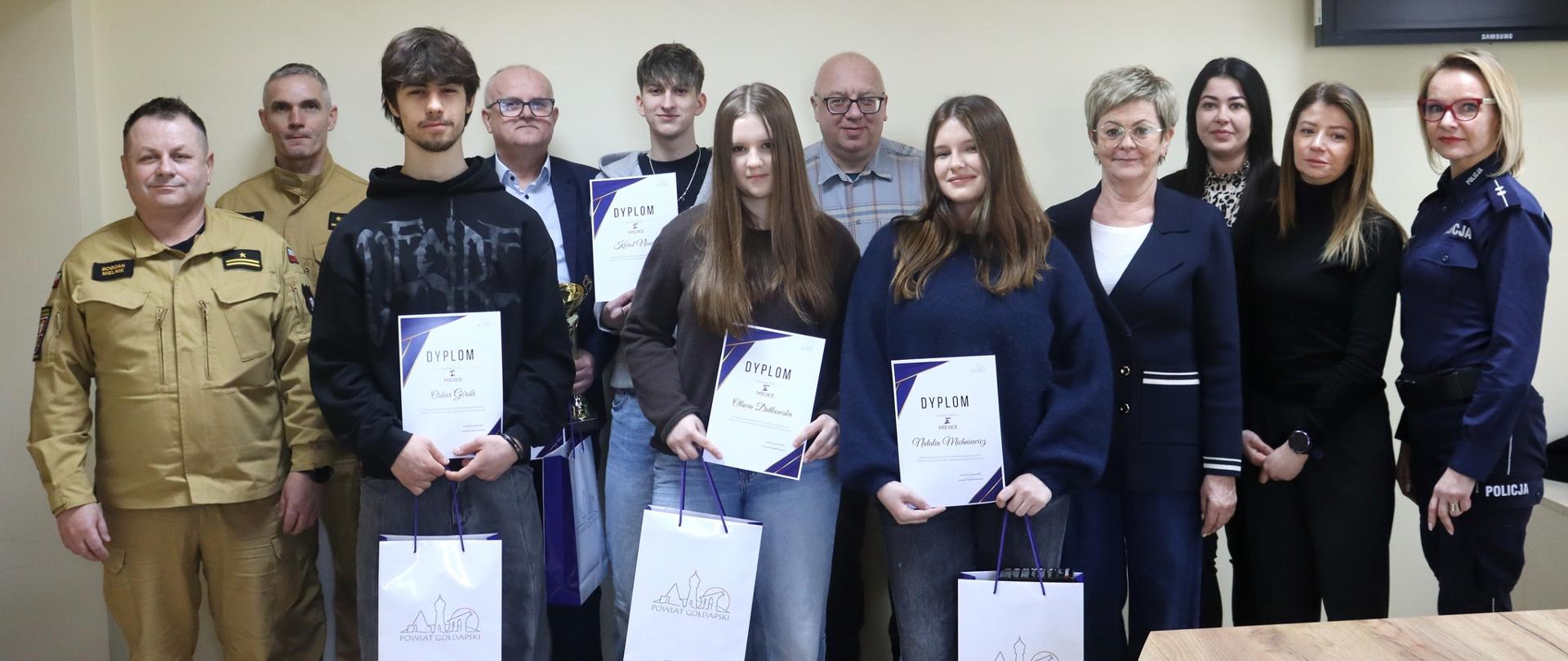 Zdjęcie przedstawia uczestników II Wojewódzkiego Konkursu Wiedzy o Ochronie Ludności i Bezpieczeństwie Powszechnym (eliminacje międzyszkolne) wraz z ich opiekunami oraz przedstawicieli Starostwa Powiatowego w Gołdapi na czele ze Wicestarostą Gołdapskim Panią Marzanną Marianną Wardziejewską (czwarta od prawej). Na obrazie obecni są również przedstawiciele zespołu sędziowskiego, w tym mł. bryg. Bogdan Mielnik i kpt. Daniel Żamojtuk z Komendy Powiatowej Państwowej Straży Pożarnej w Gołdapi