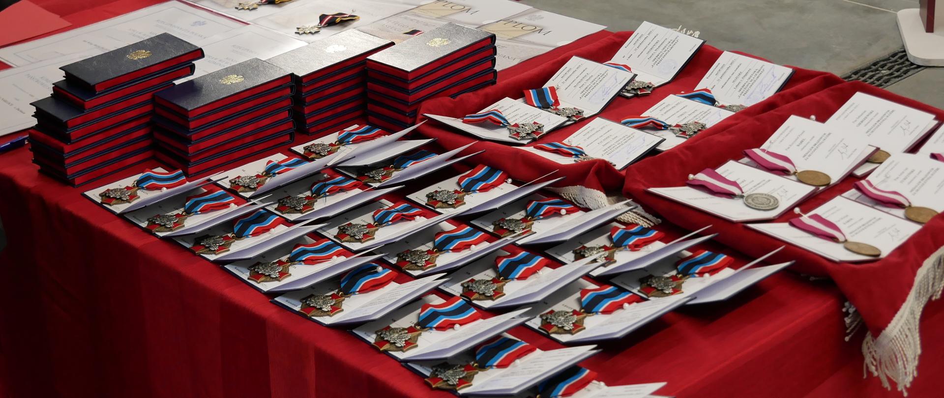 Wyróżnienia i medale leżą na stole przykrytym czerwonym obrusem