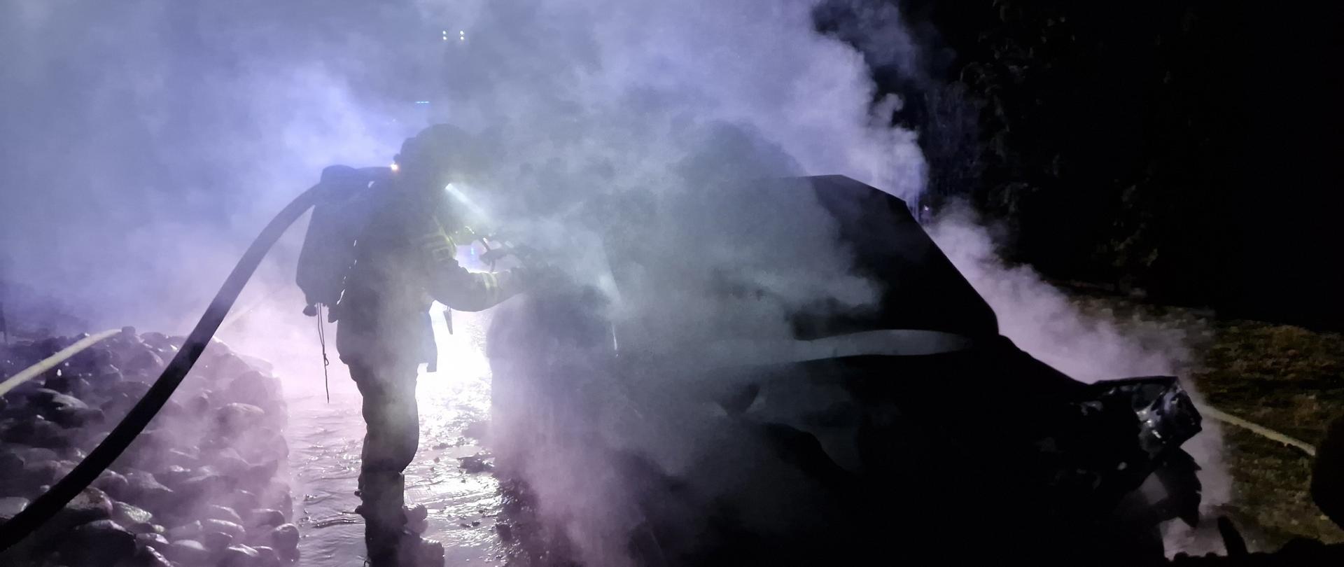 Strażak gasi pojazd, jest dym i noc