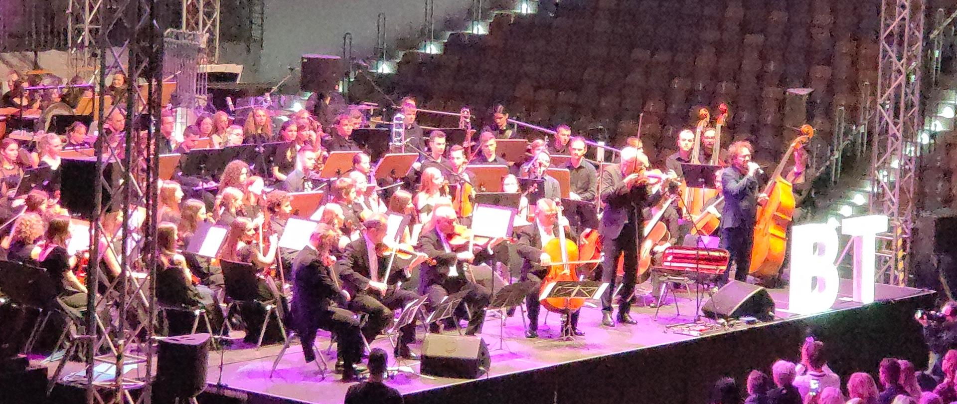 Zdjęcie przedstawia orkiestrę i muzyków występujących na koncercie finałowym opolskiego Banku Talentów w Stegu Arena 19.11.2022