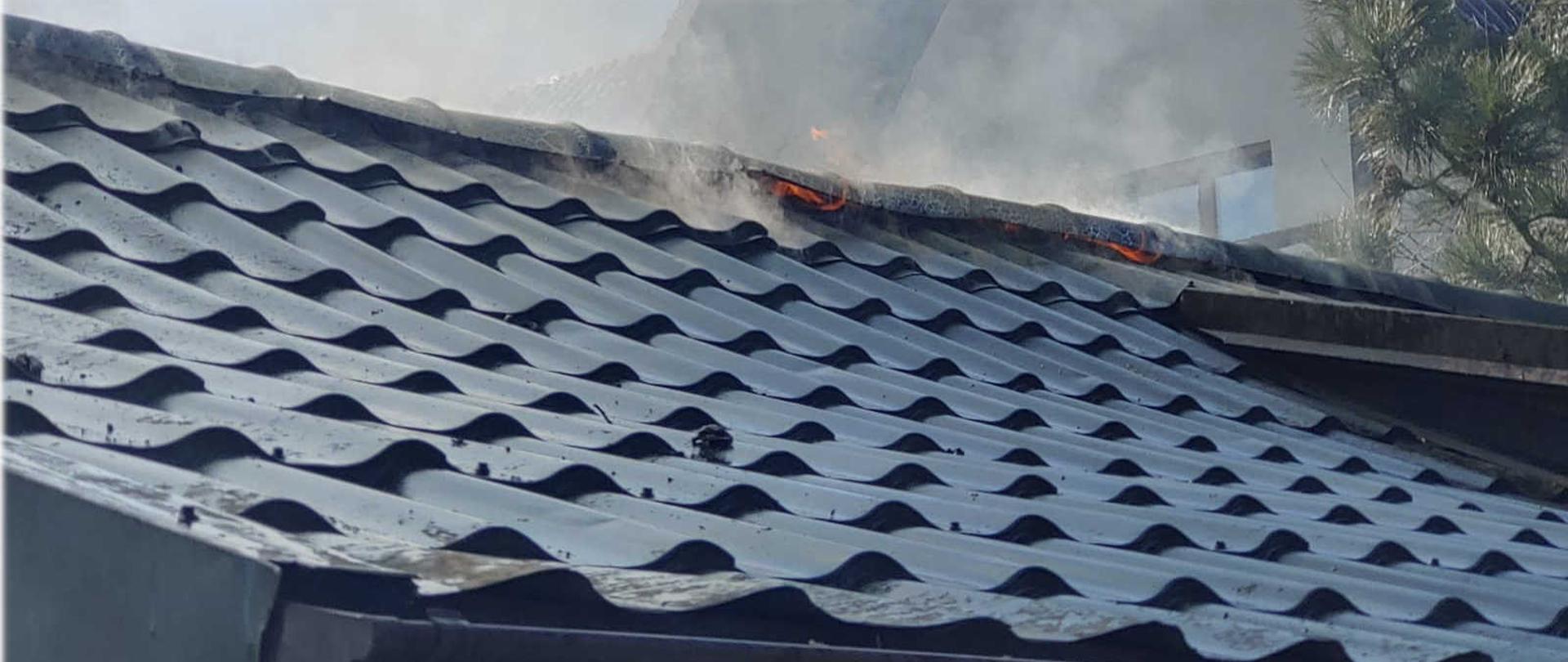 Dach budynku z wychodzącymi płomieniami na kalenicy.