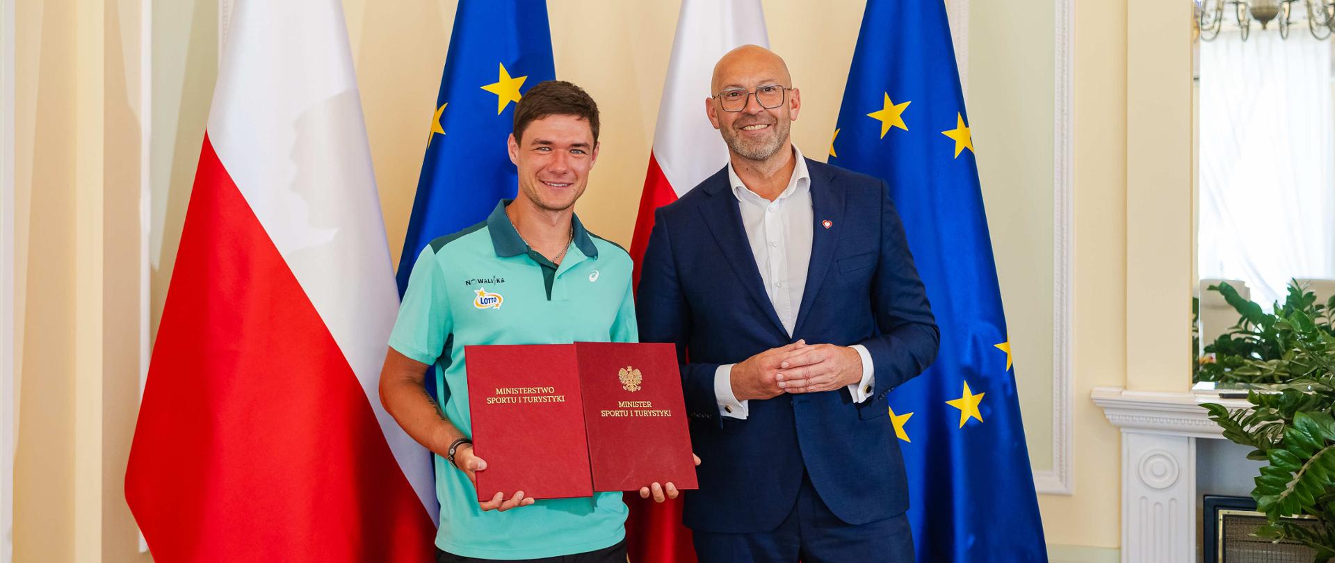 Kamil Majchrzak i minister sportu i turystyki Jakub Rutnicki na tle flag Polski i UE.