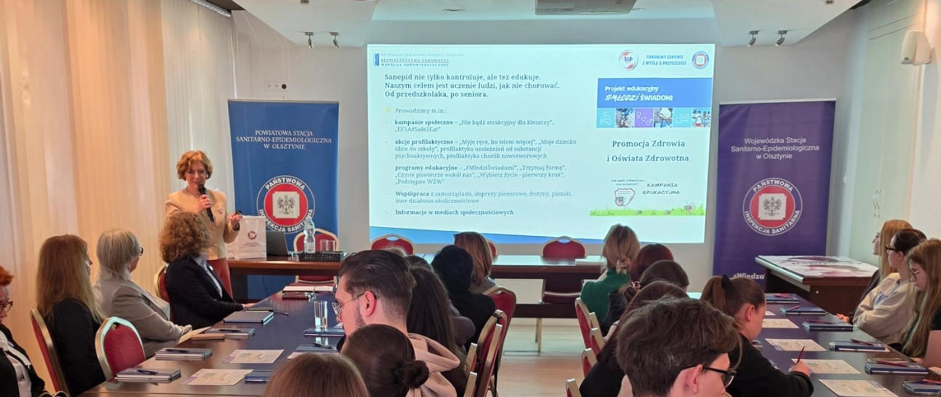 Dzień Otwarty Państwowej Inspekcji Sanitarnej. Sala wypełnina słuchaczami. Na stołąch leżą materiały szkoleniowe. 