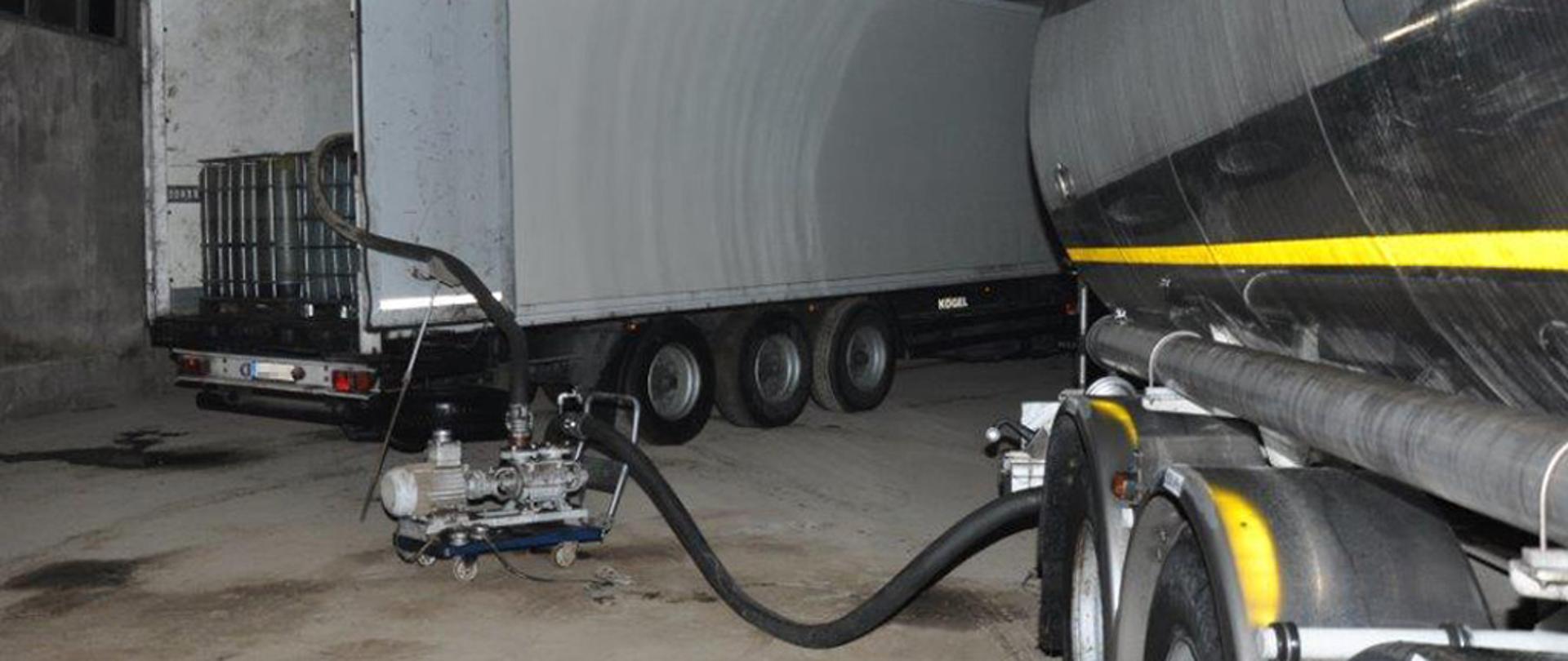 Wnętrze hali z naczepą, cysterną i pompa.