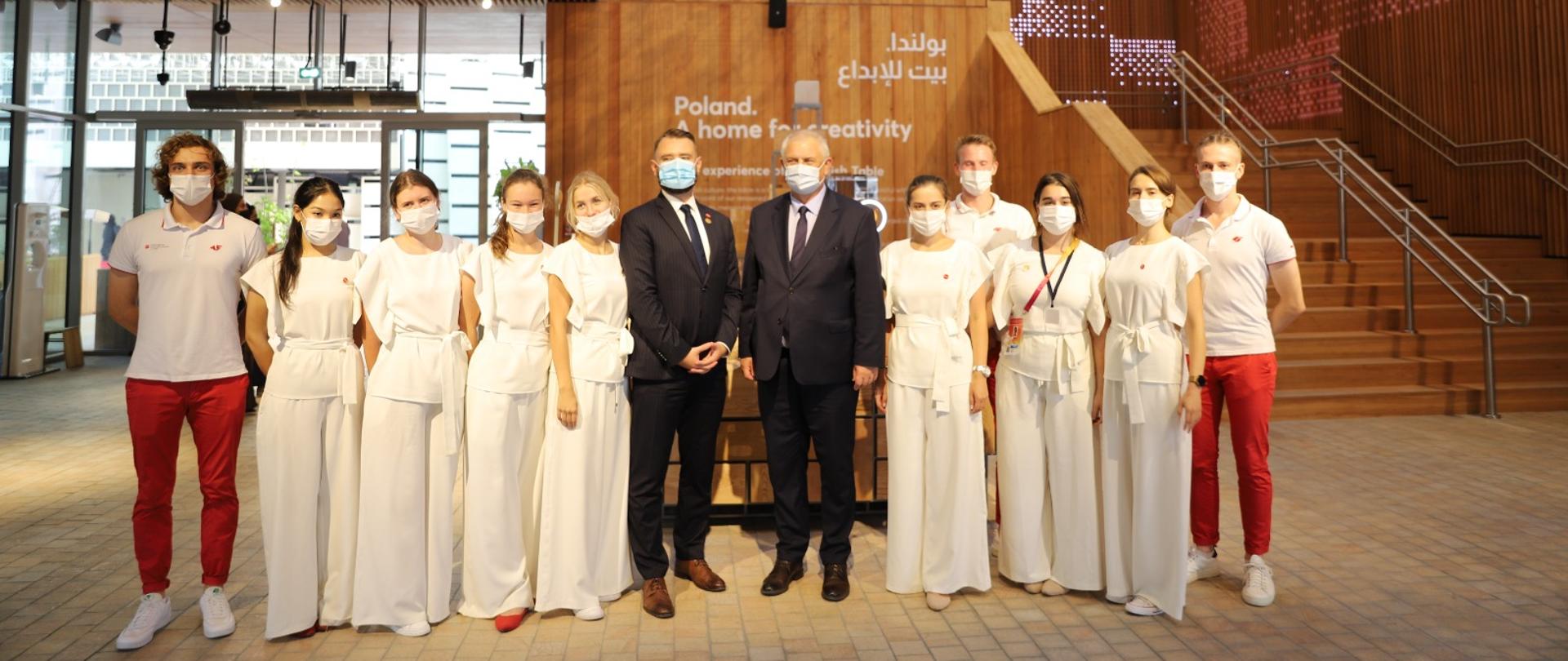 Wiceminister Grzegorz Piechowiak stoi w środku wśród młodych ludzi ubranych na biało i biało-czerwono. 