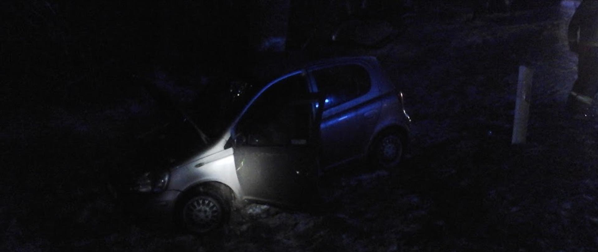 Samochód osobowy stojący na kołach na zaśnieżonym poboczu jezdni. Drzwi kierowcy i przednia maska otwarte.