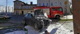 Widać uszkodzony przód samochodu, w koło znajduje się piana gaśnicza, po lewej samochód Policji, z tyłu samochód Straży Pożarnej