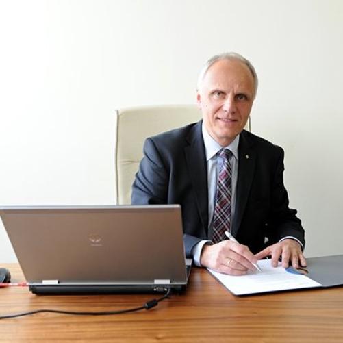 Mężczyzna w garniturze siędzący przy biurku podczas podpisywania dokumentów.