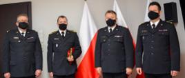 Zdjęcie przedstawia czterech strażaków, którzy stoją na tle flag Polski. Strażak mł. asp. Mieczysław Kaczmarczyk stoi drugi od lewej trzymając okolicznościową statuetkę strażaka.