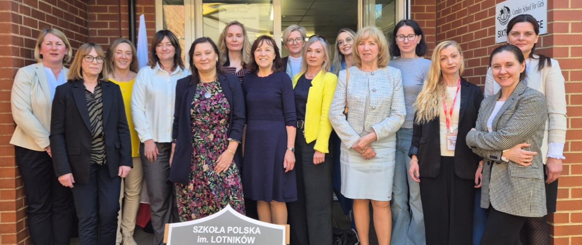 Zdjęcie grupowe. Kilka osób przed wejściem do budynku pozuje do zdjęcia.