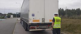 Umundurowany inspektor warmińsko-mazurskiej ITD stoi z tyłu naczepy ciężarowej i kontroluje jej stan techniczny.