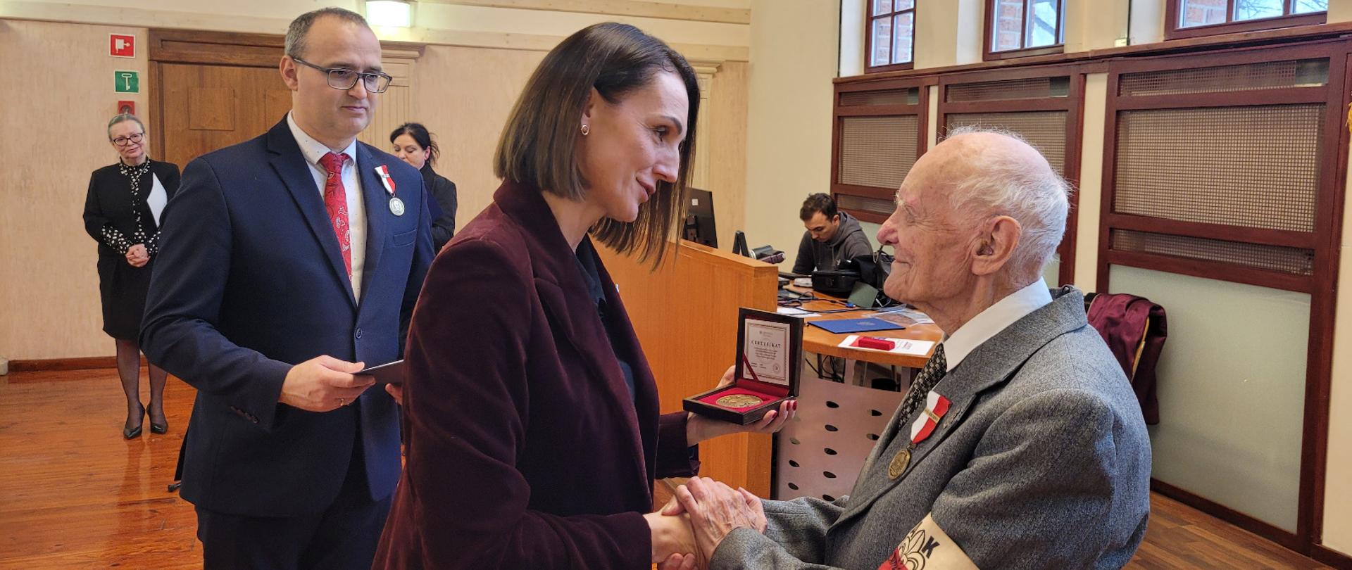 kobieta ( wojewoda) wręcza medal starszemu mężczyźnie żołnierzowi Armii Krajowej