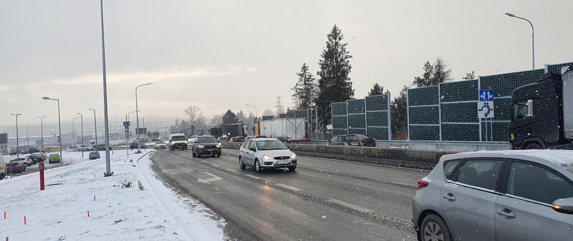 droga dwujezdniowa, jadą samochody, pada śnieg, po prawej stronie są ekrany akustyczne