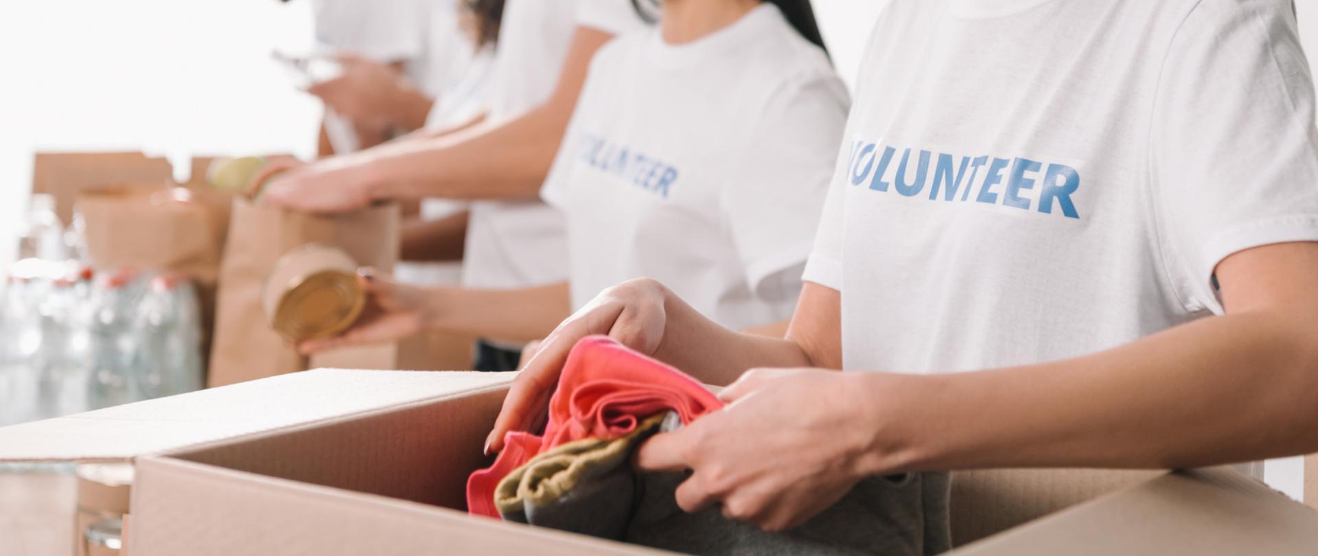 Na zdjęciu są wolontariusze, którzy pakują ubrania, żywność oraz wodę do kartonów oraz toreb.