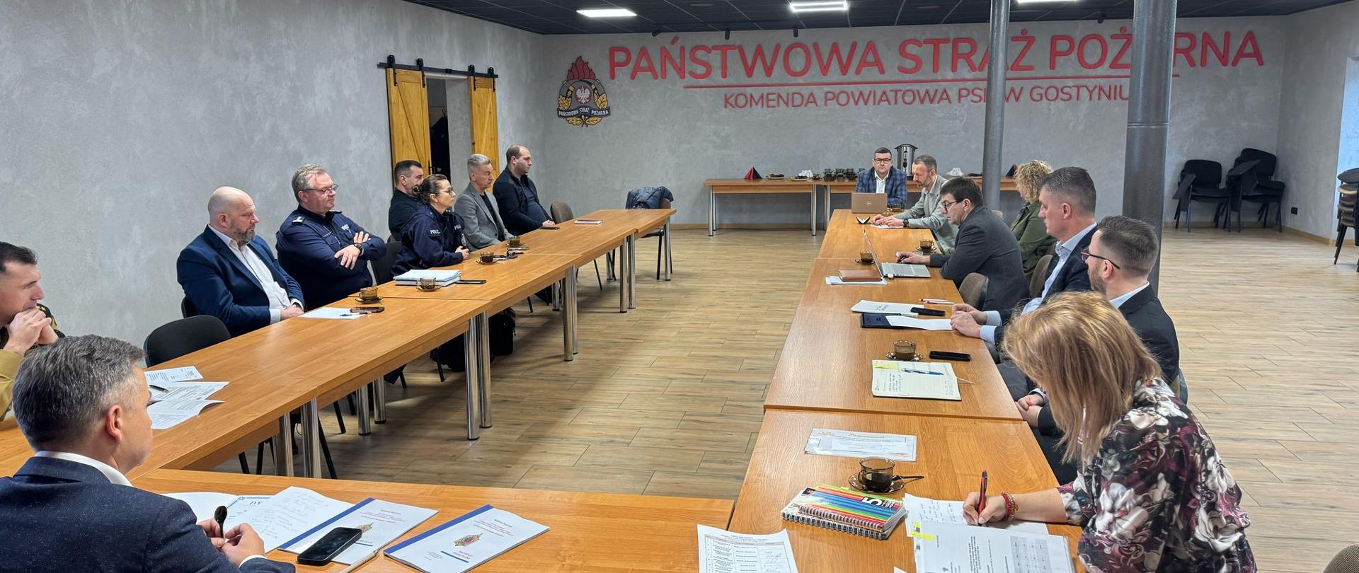 Członkowie komisji siedzą przy stołach na sali