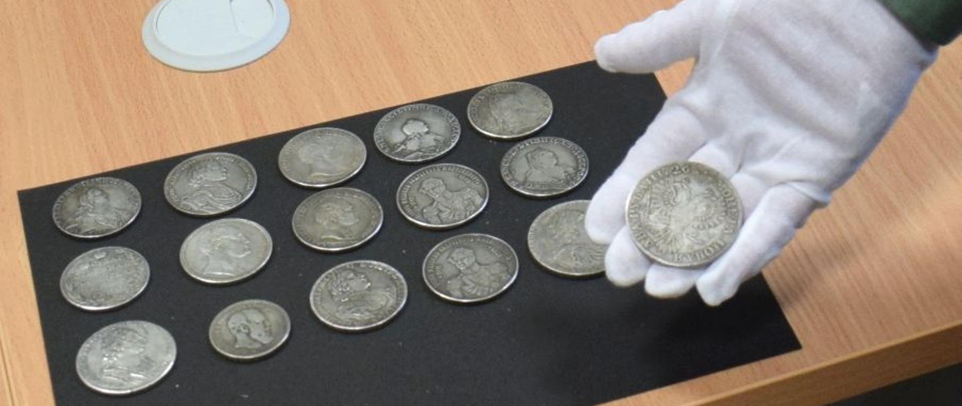 Monety rozłożone na stole, jedna na dłoni w rękawiczce.