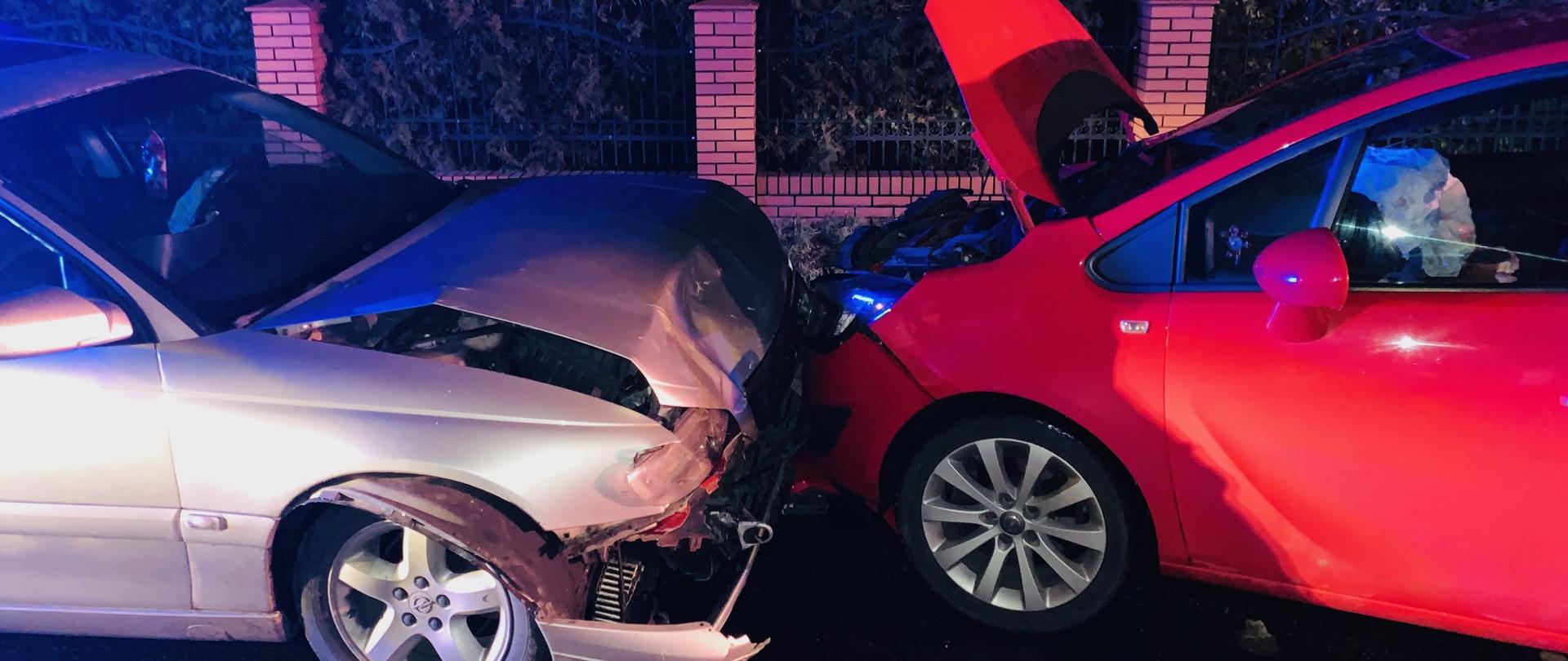 Dwa samochody osobowe po czołowym zderzeniu. Po lewej samochód koloru srebrnego, po prawej czerwony.