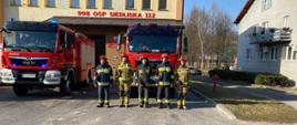 Na zdjęciu widoczni są strażacy Posterunku Czasowego w Siedliskach podczas apelu upamiętniającego strażaków z Ukrainy. W tle widoczny jest budynek remizy strażackiej w Siedliskach oraz stojące przed nim dwa samochody bojowe.