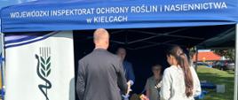 Pracownicy Inspekcji przy stoisku promocyjnym prezentujący ulotki informacyjne uczestnikom wydarzenia.