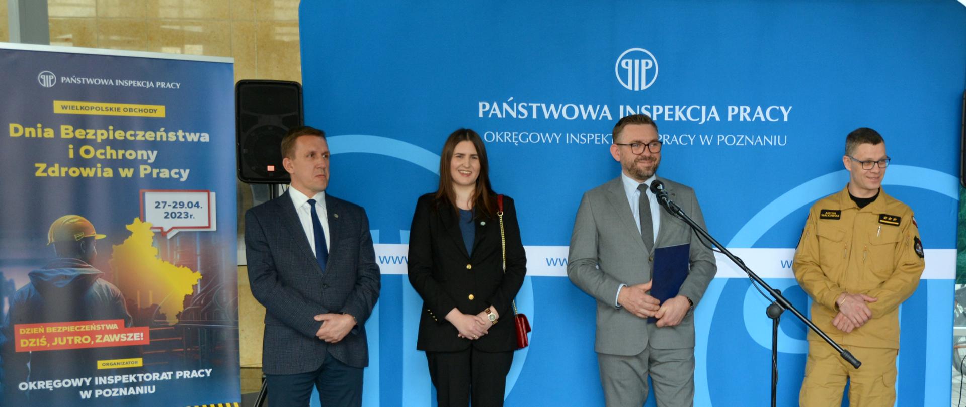 cztery osoby stoją obok siebie na tle niebieskiego baneru