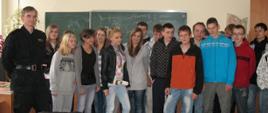 Zdjęcie przedstawia gimnazjalistów w klasie stojących przed tablicą obok stoi strażak
