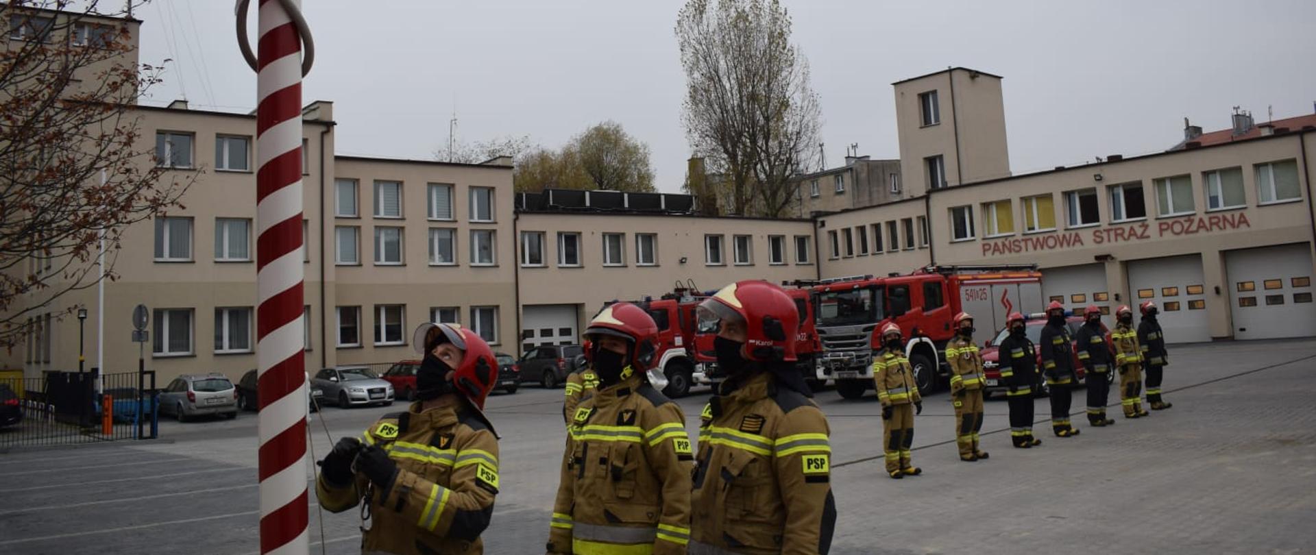 Uroczysta zbiórka na placu KP PSP Tczew strażaków w umundurowaniu specjalnym, w tle wozy strażackie - podniesienie flagi państwowej.