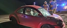Zdjęcie przedstawia samochód osobowy po wypadku. Obok stoi trzech strażaków i policjant