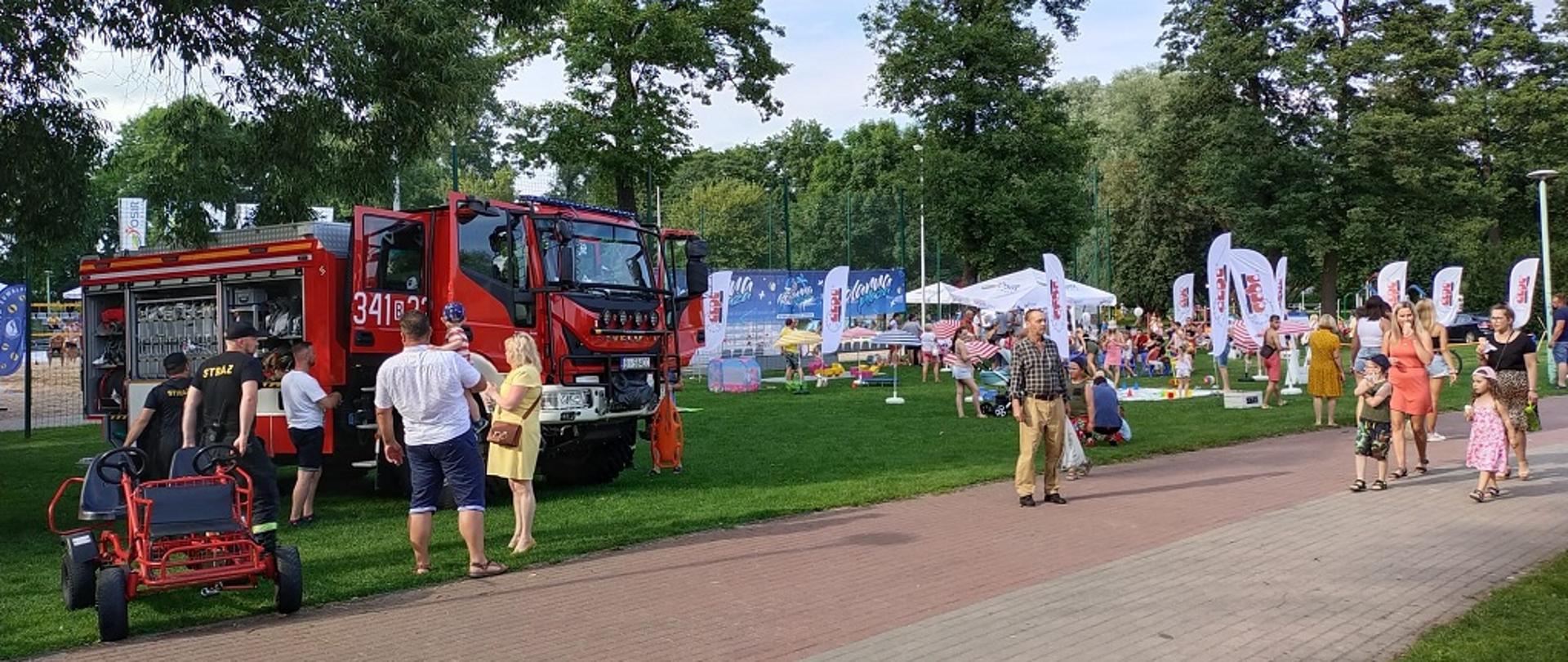 Czerwony samochód strażacki z osobami które go oglądają