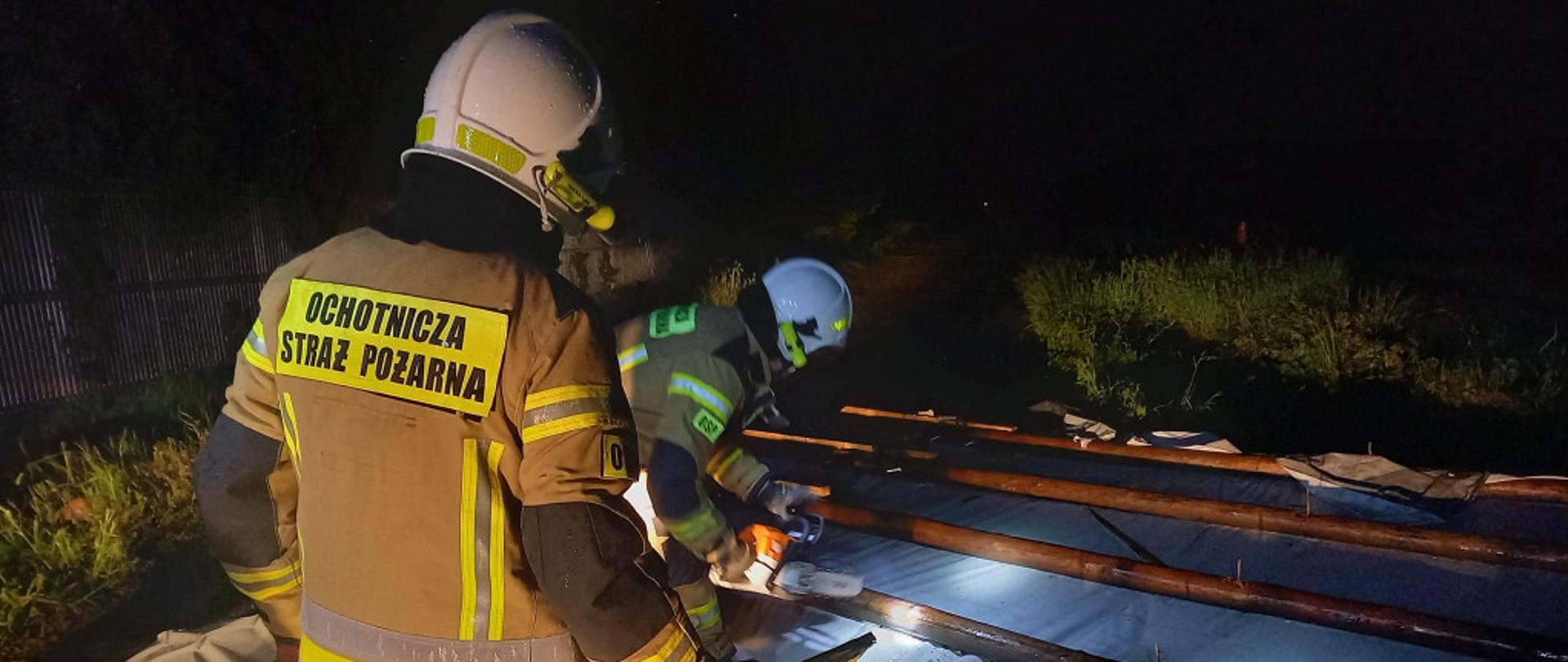 Strażacy przecinają uszkodzony dach pilarką.