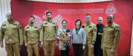 Na zdjęciu funkcjonariusze i pracownicy cywilni KP PSP w Jędrzejowie. Dwóch pracowników cywilnych trzyma w ręku okazałe bukiety kolorowych kwiatów oraz listy gratulacyjne.