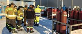 Zdjęcie przedstawia strażaków uczestniczących w warsztatach oraz pracownika firmy AirLiquide Polska Sp. z o.o. w trakcie omówienia postępowania w przypadku uszkodzenia butli z acetylenem.