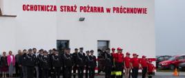 Zdjęcie przedstawia strażaków podczas uroczystości otwarcia nowej remizy jednostki OSP Próchnowo.
W tle budynek remizy.
