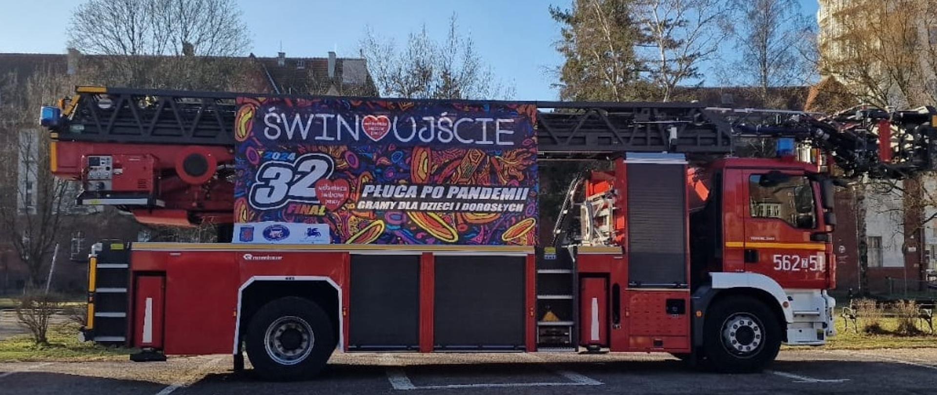 Zdjęcie przedstawia drabinę mechaniczną z wywieszonym banerem z logiem Wielkiej Orkiestry Świątecznej Pomocy.