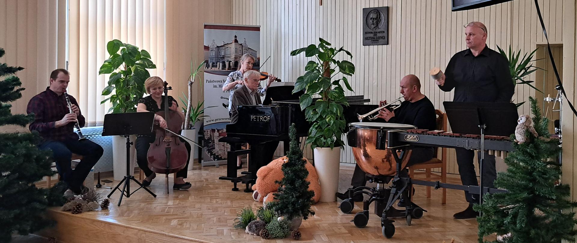 Na scenie od lewej: klarnecista, wiolonczelistka, skrzypaczka, pianista, trębacz, perkusista z kotłami i ksylofonem. Wykonują wspólnie utwór. 