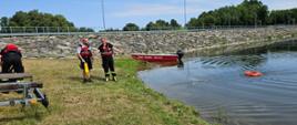 Ćwiczący strażak i policjant po rzuceniu koła ratowniczego na zbiornik wodny.