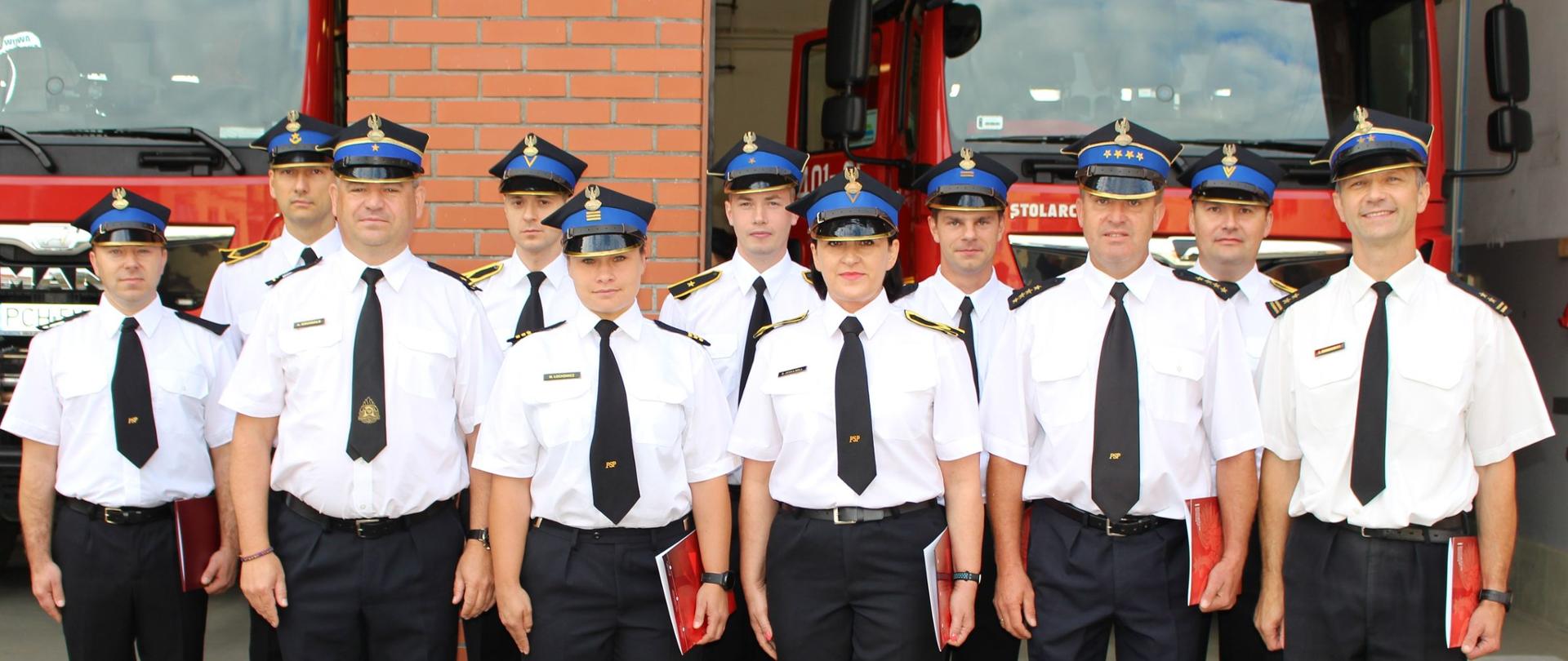 Zdjęcie przedstawia uroczyste wręczenie awansów i wyróżnień dla strażaków.
W tle plac Komendy, inni strażacy i budynki.
