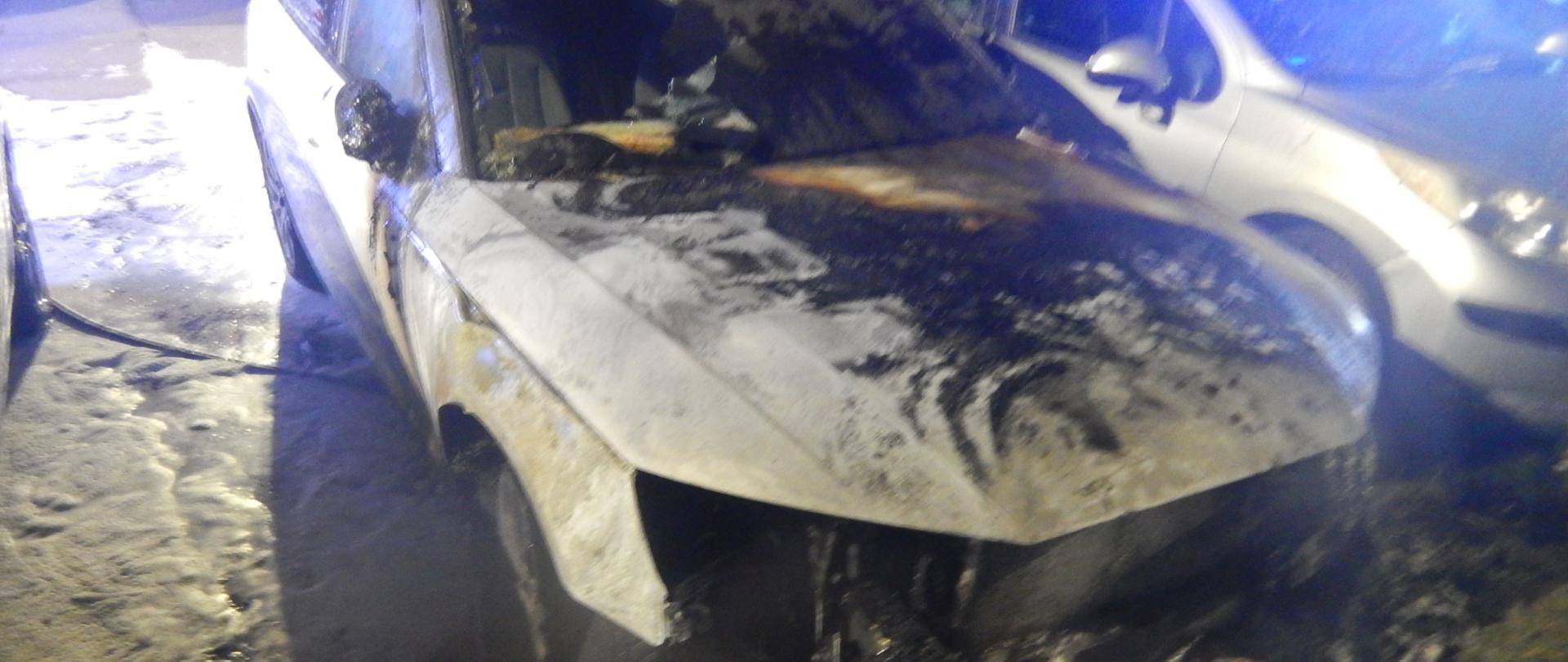 Zdjęcie przedstawia spaloną komorę silnika samochodu marki Audi koloru białego.