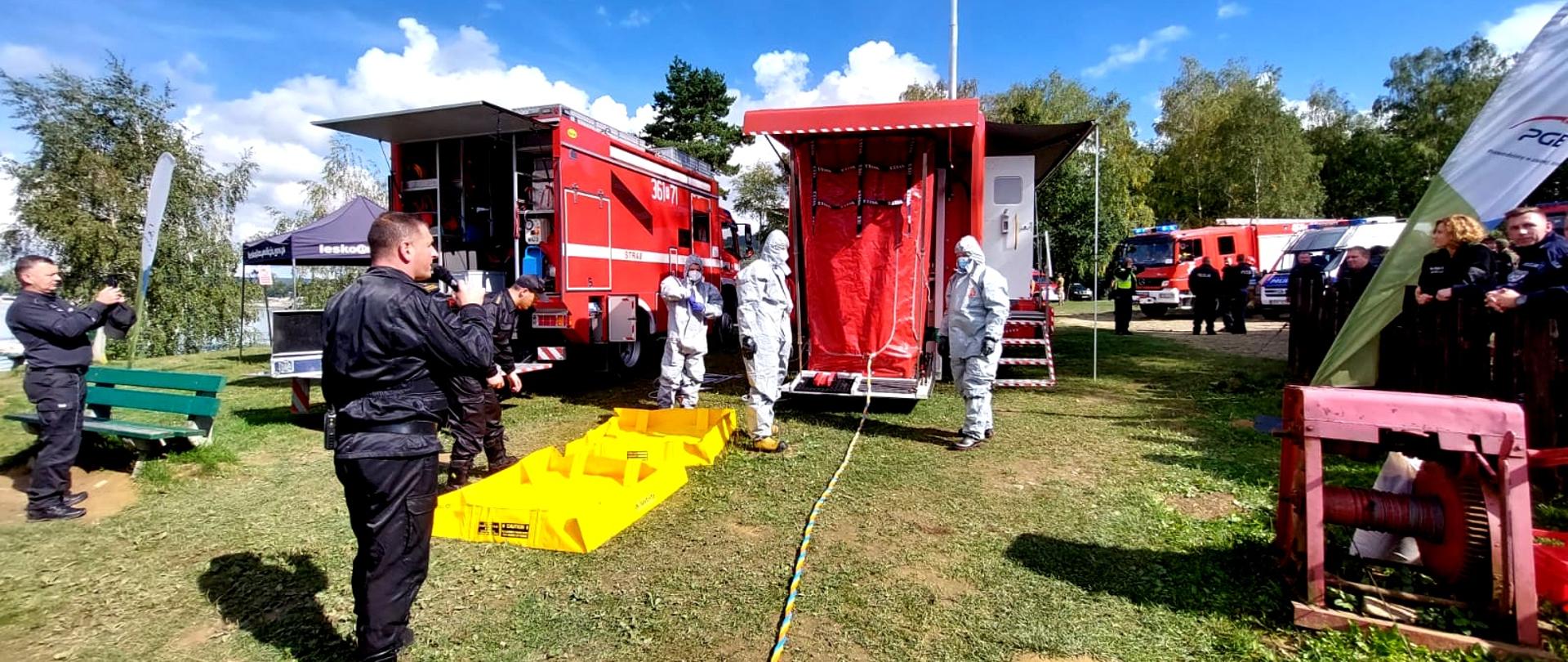 Zdjęcie zrobione na zewnątrz, podczas ćwiczeń. Na fotografii strażacy uczestniczący w manewrach