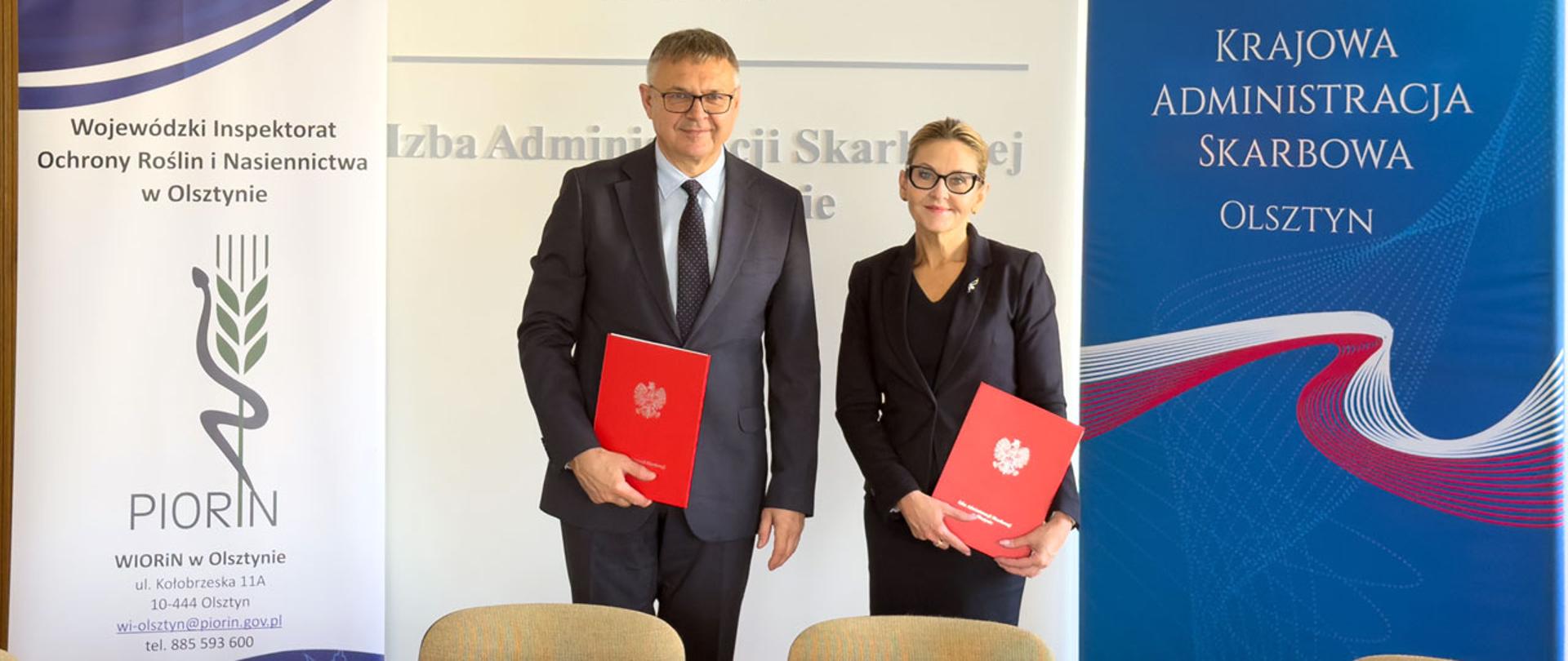 Katarzyna Dębowska i Jarosław Orłowski stoją obok siebie, trzymając podpisane porozumienia w czerwonych okładkach.