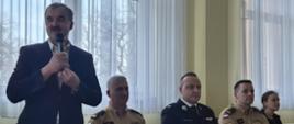 Na zdjęciu widoczny wójt gminy Lipinki podczas przemówienia na naradzie operacyjnej dla naczelników OSP i komendantów gminnych ZOSP RP z terenu powiatu gorlickiego. obok przy stole prezydialnym siedzą komendant powiatowy PSP w Gorlicach ubrany w ubranie służbowe koloru pisakowego,zastępca komendanta powiatowego w Gorlicach ubrany w ubranie służbowe koloru pisakowego, prezes powiatowy Związku Ochotniczych Straży Pożarnych Rzeczypospolitej Polskiej w Gorlicach ubrany w ubranie wyjściowe koloru granatowego.