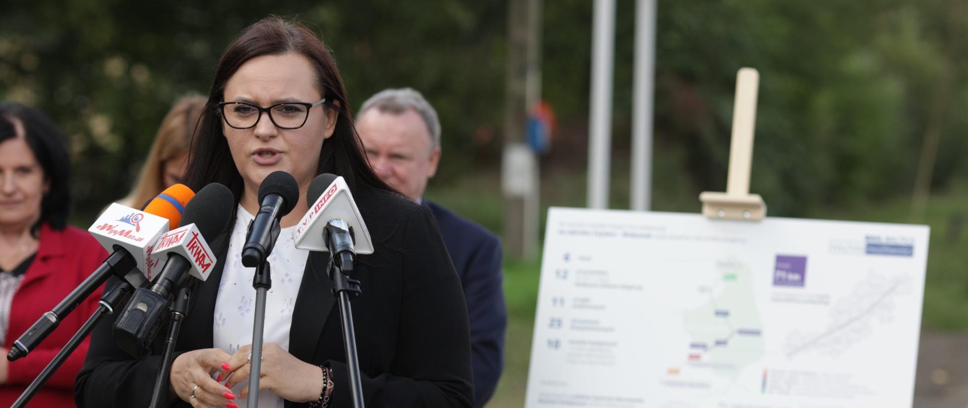 Minister Jarosińska-Jedynak stoi na peronie kolejowym, mówi do mikrofonu