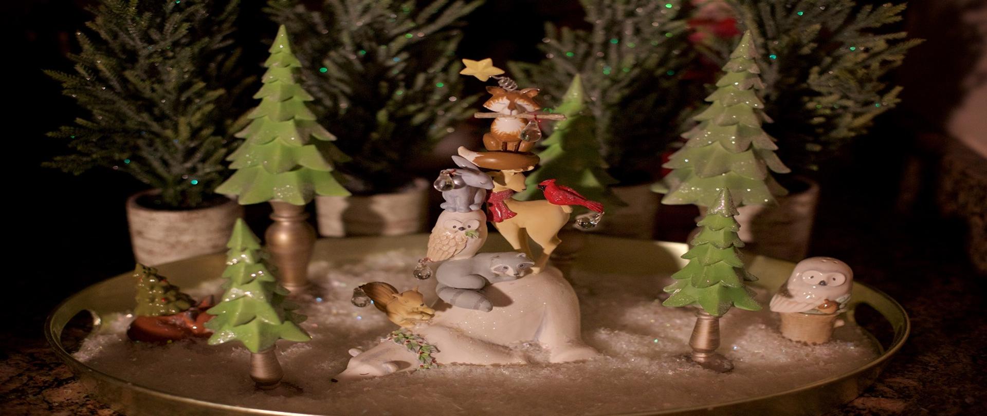 Zdjęcie przedstawia figurki zwierząt leśnych w otoczeniu sztucznych i miniaturowych żywych choinek 