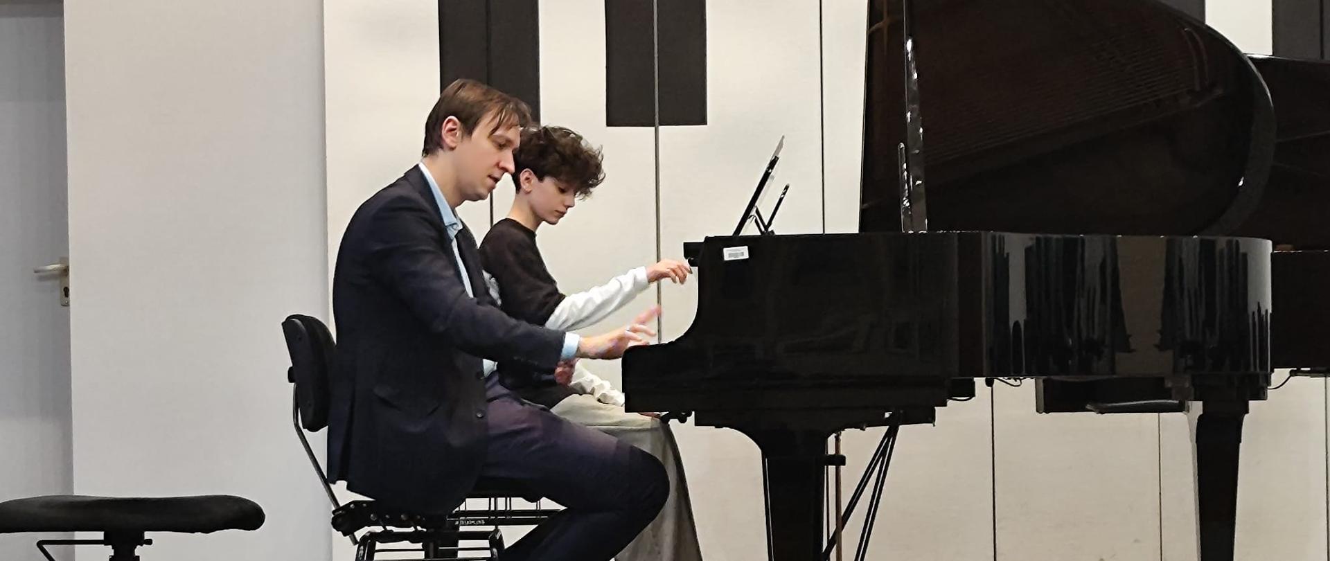 Mężczyzna i chłopak grają na dwóch fortepianach.