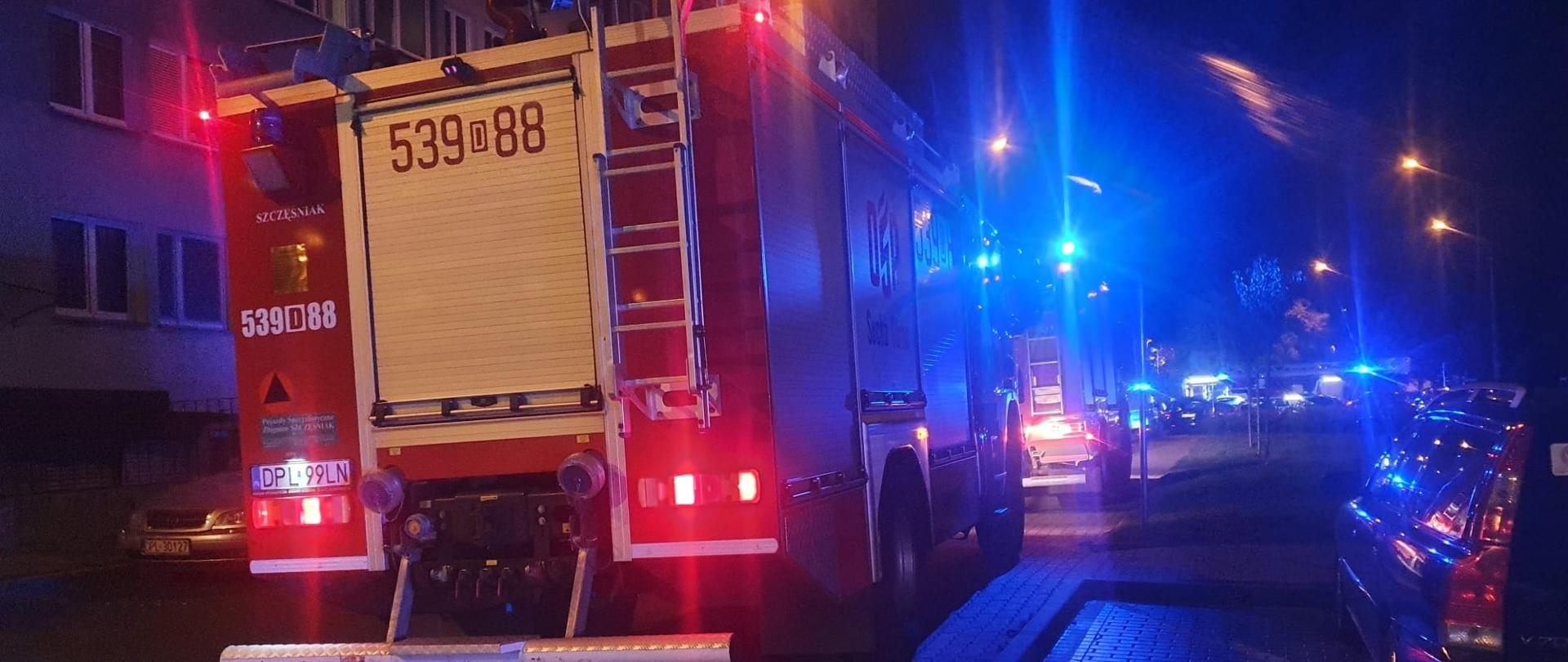 Auto strażackie na sygnałach stoi koło budynku mieszkalnego w nocy