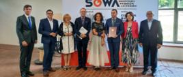 Zdjęcie zbiorowe - grupa ośmiu osób stoi pod ścianką z napisem SOWA.