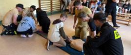 Zdjęcie przedstawia strażaków przekazujących wiedzę młodzieży z zakresu pierwszej pomocy